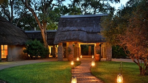 A thatched-roof building with a stone pathway leading to it, surrounded by greenery. - Imbali Safari Lodge (Imbali Concession)