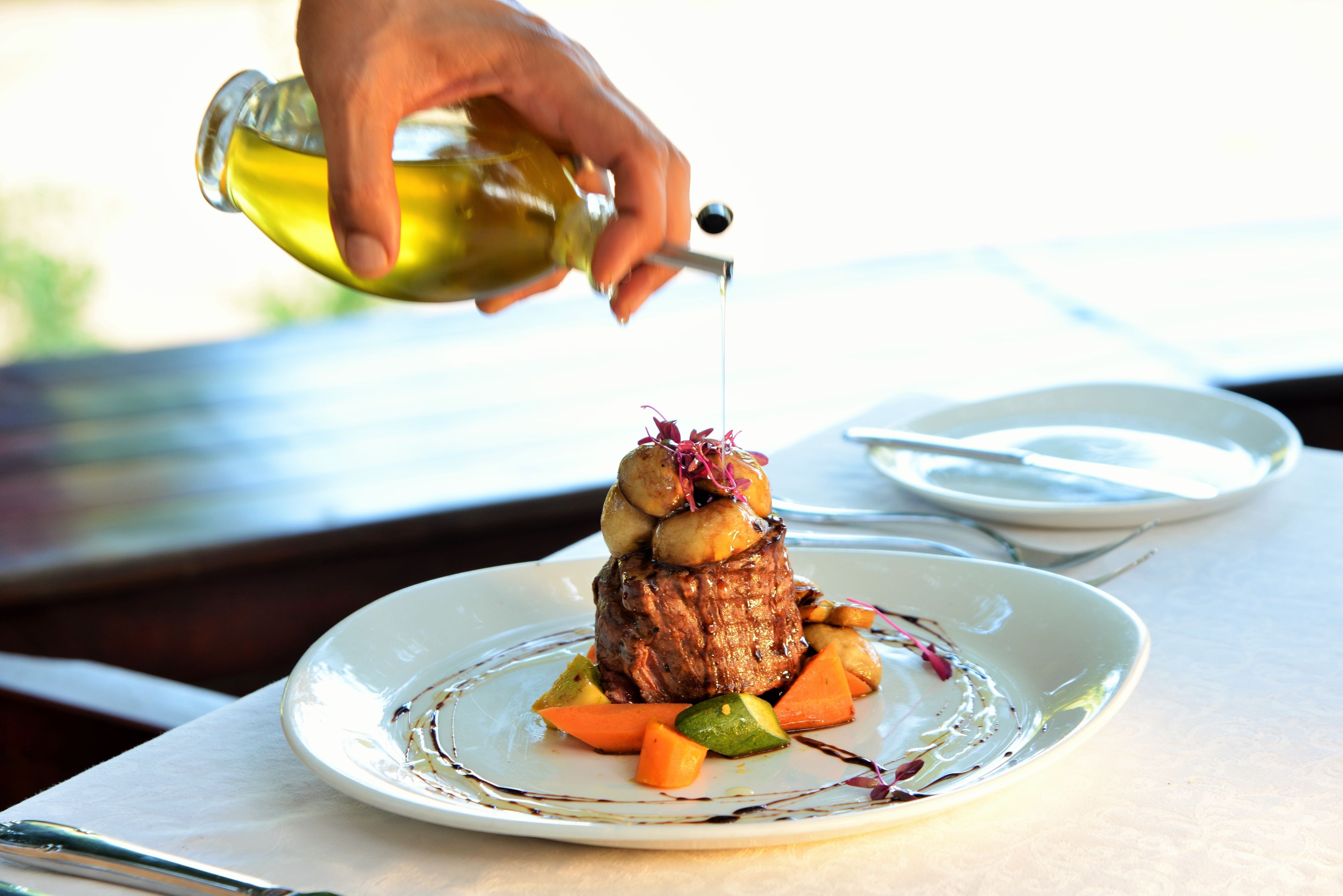 A plate with a steak topped with potatoes and vegetables, being drizzled with sauce.