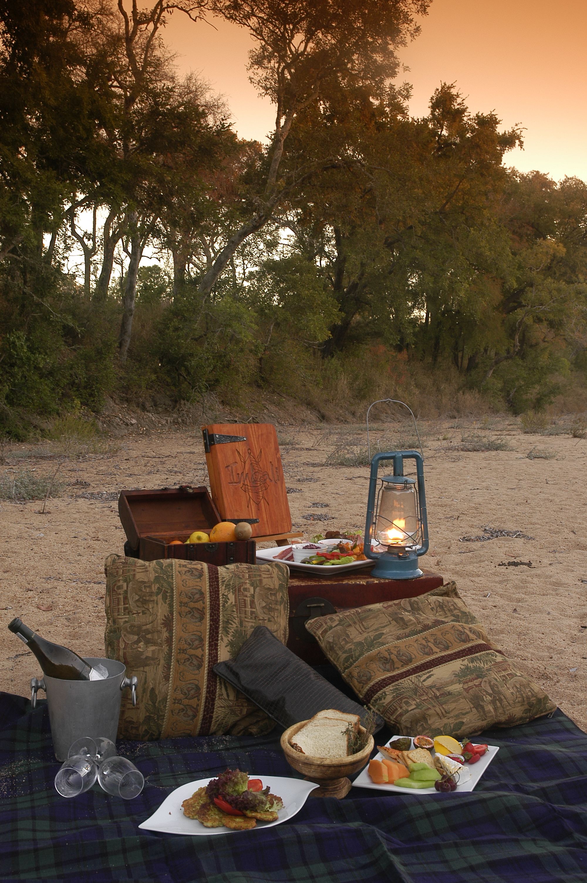A picnic setup on a blanket with a lantern, a wooden box, and a metal bucket.