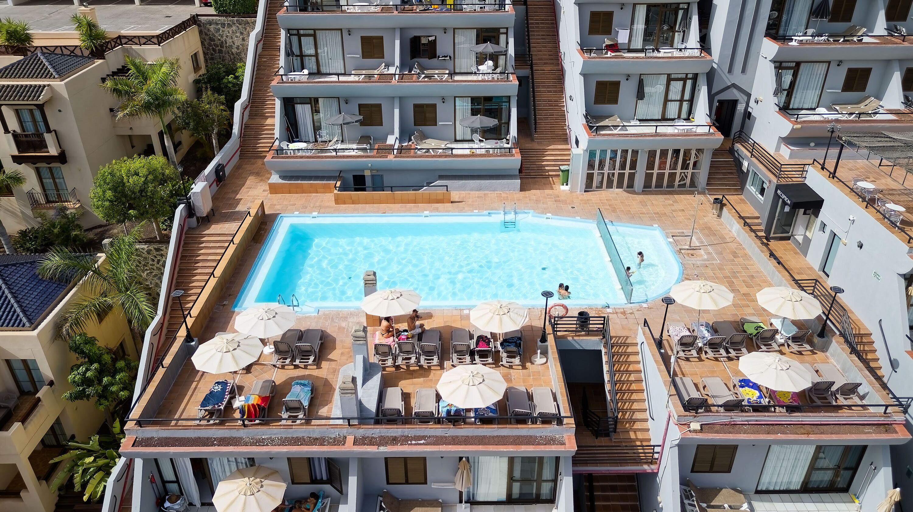 Un área de piscina en la azotea con múltiples sillas de descanso y sombrillas, rodeada de edificios residenciales.