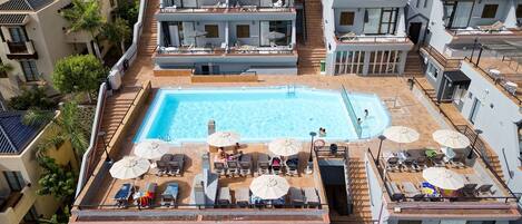 A rooftop pool area with multiple lounge chairs and umbrellas, surrounded by residential buildings.