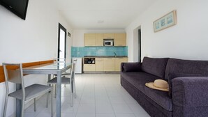 Un espace de vie compact comprenant un coin cuisine, un coin repas avec une table et des chaises, et un canapé sur lequel est posé un chapeau.