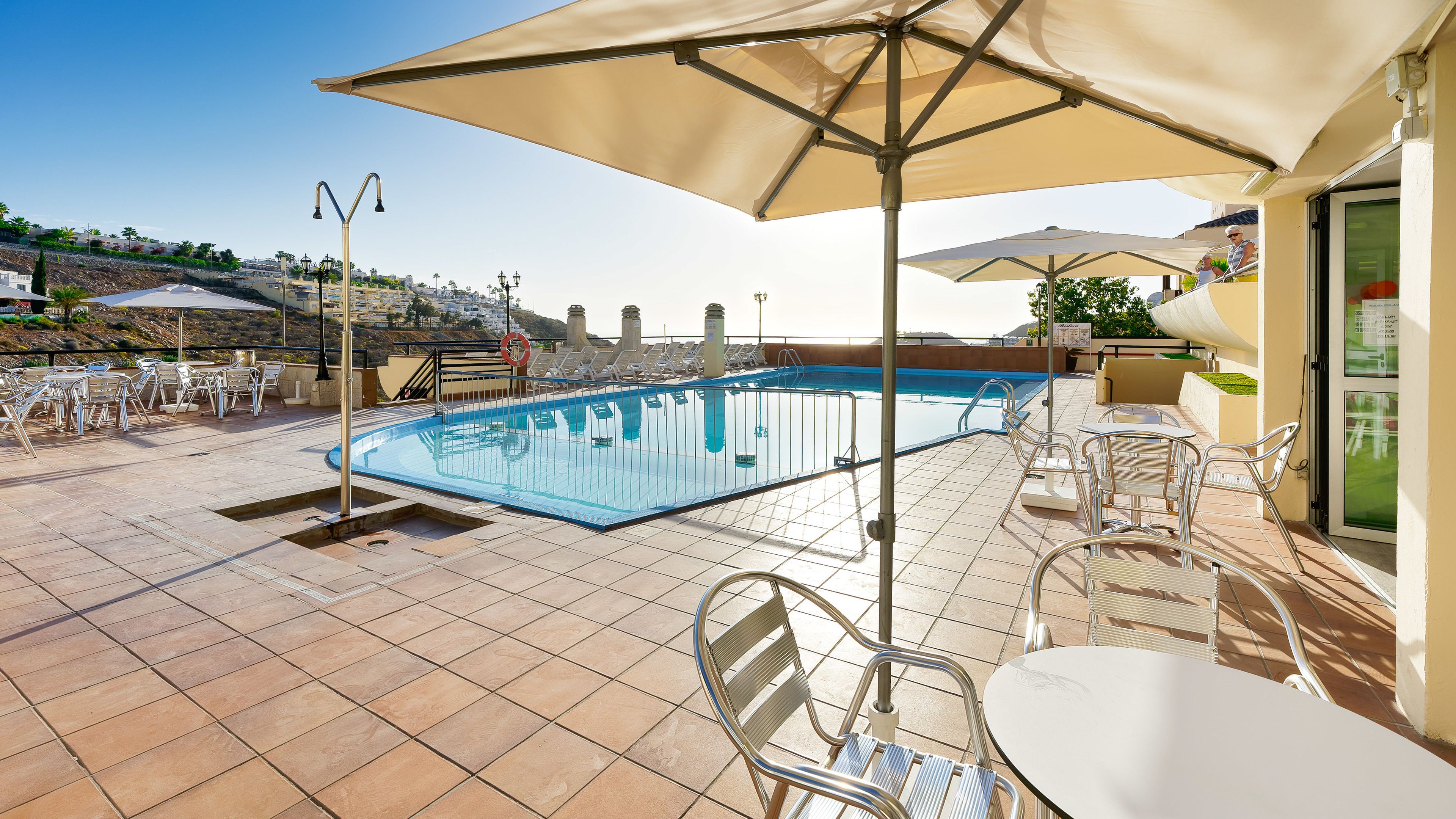 Uma área à beira da piscina com piscina, espreguiçadeiras e guarda-sóis.
