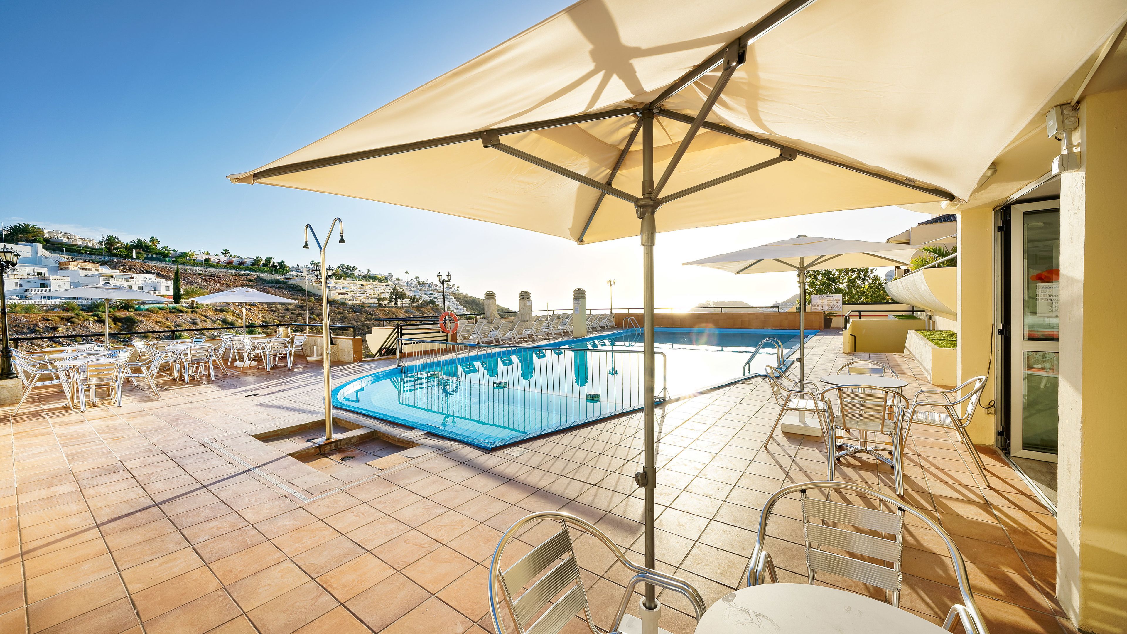 Zona de piscina al terrat amb paviment de rajoles, seients relaxants i ombrel·les.