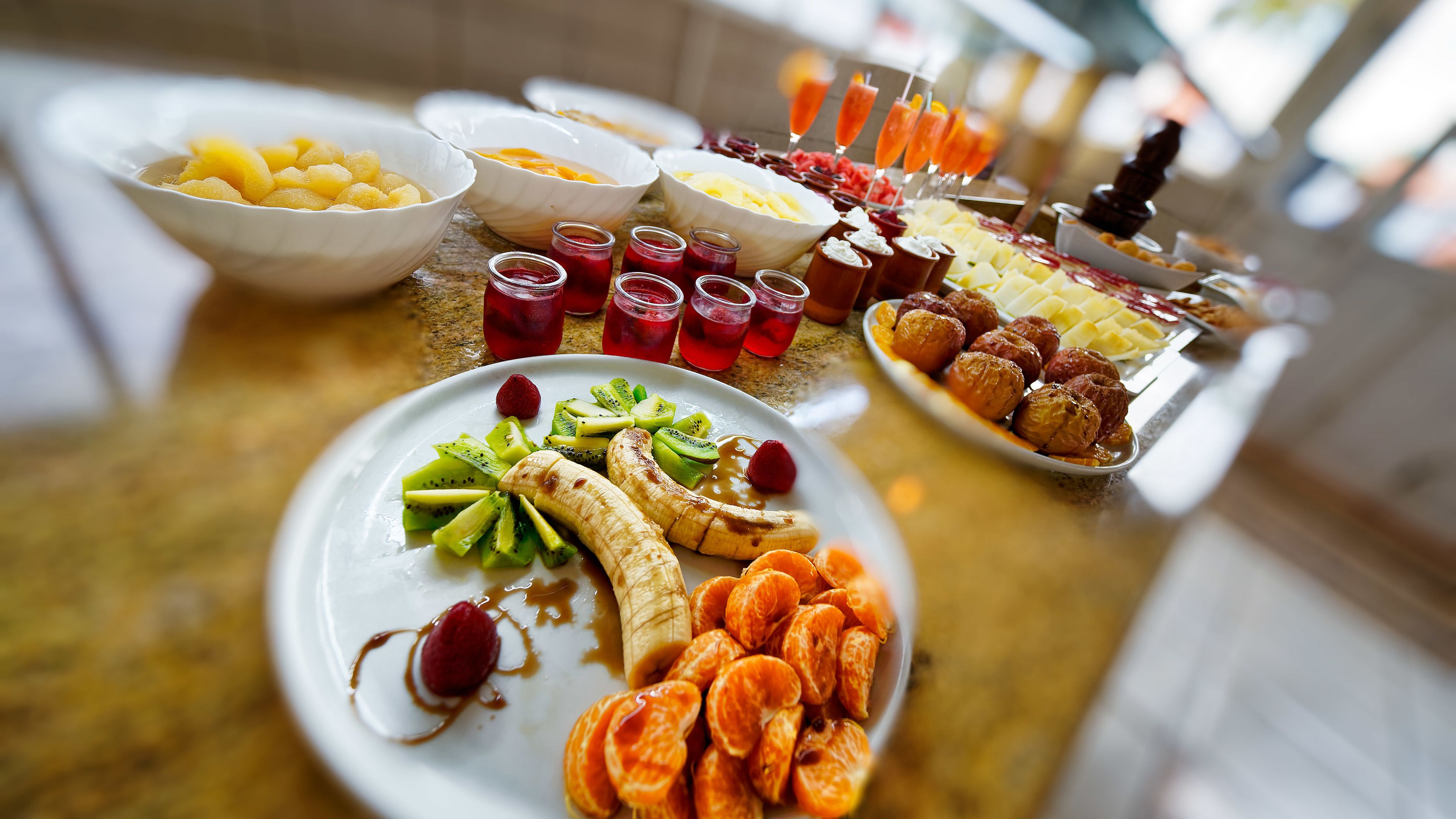 A buffet table with various fruits, desserts, and beverages.