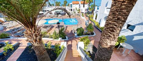 A resort with a swimming pool, palm trees, and a view of the ocean.