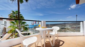 A balcony with white plastic chairs, a small round table, and a view of the sea and hills. - Ura Nido del Águila (Mogan)