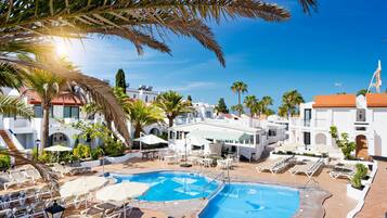 Een resort met een zwembad, ligbedden en palmbomen.
