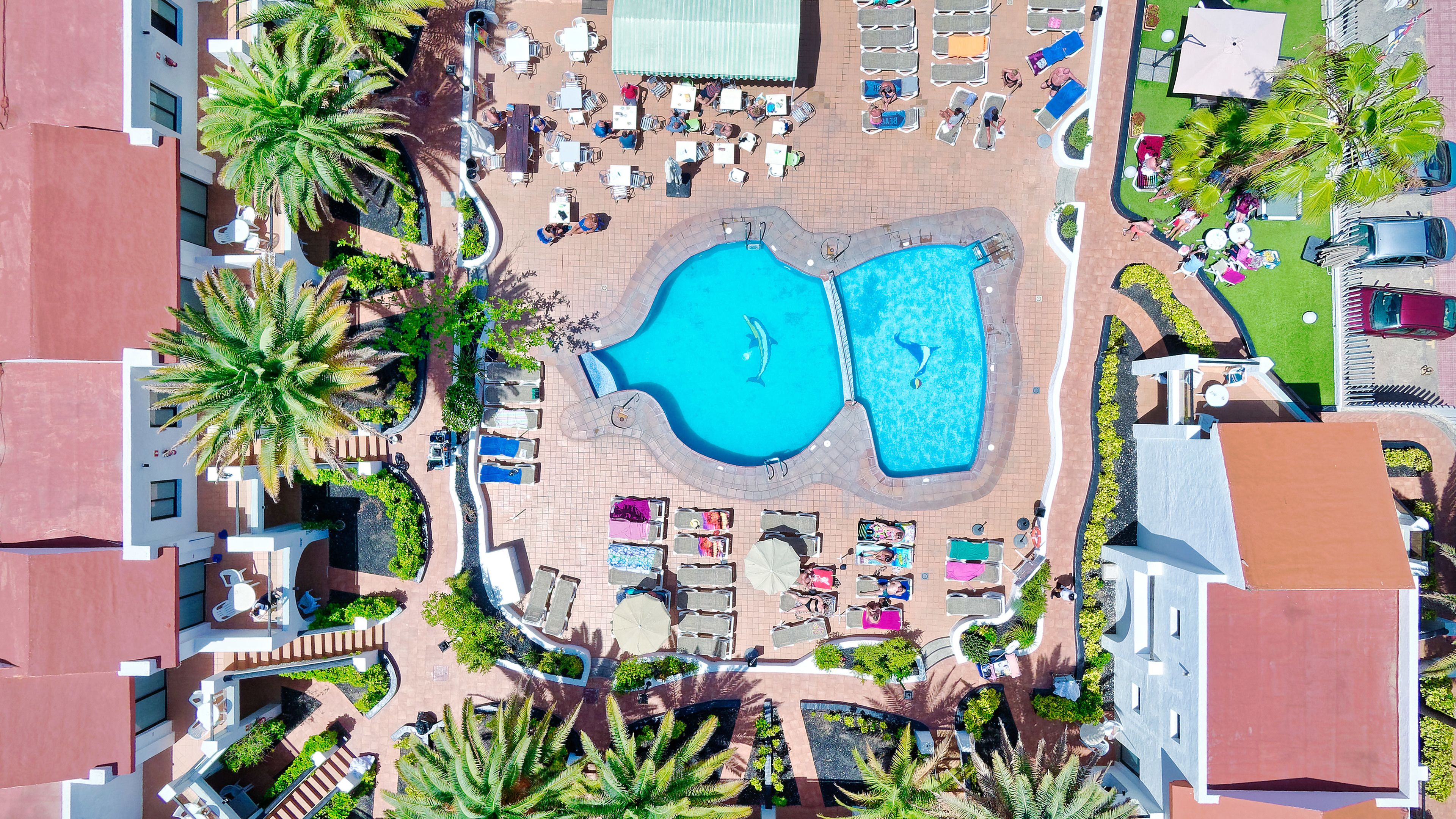 Vista aérea de um resort com uma piscina central, áreas de descanso e vegetação ao redor.