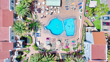 Vista aérea de um resort com uma piscina central, áreas de descanso e vegetação ao redor.