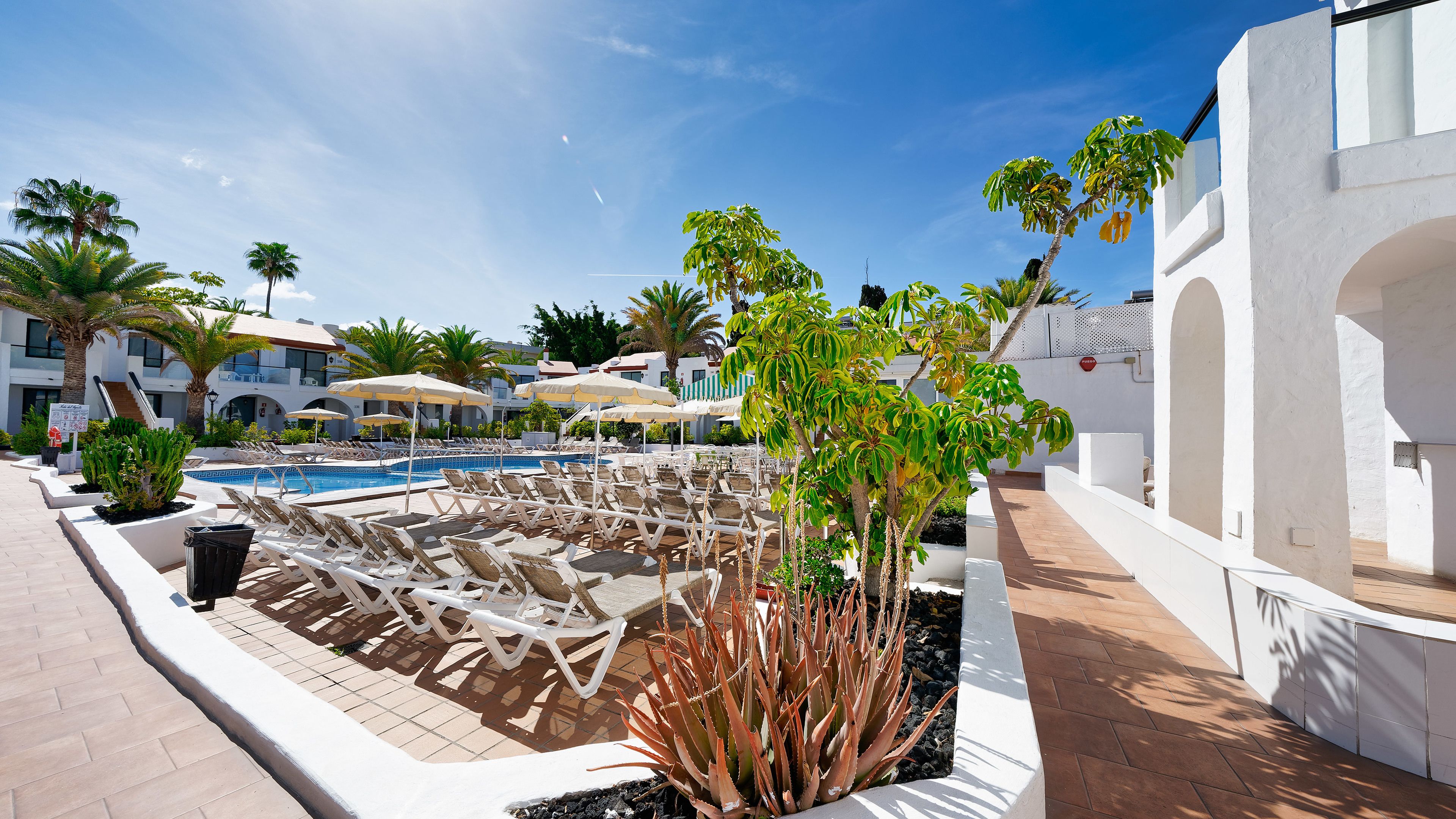 A poolside area with lounge chairs, a swimming pool, and a white building with arches.