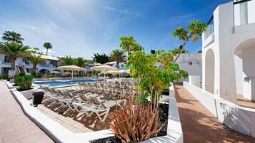 A poolside area with lounge chairs, a swimming pool, and a white building with arches.