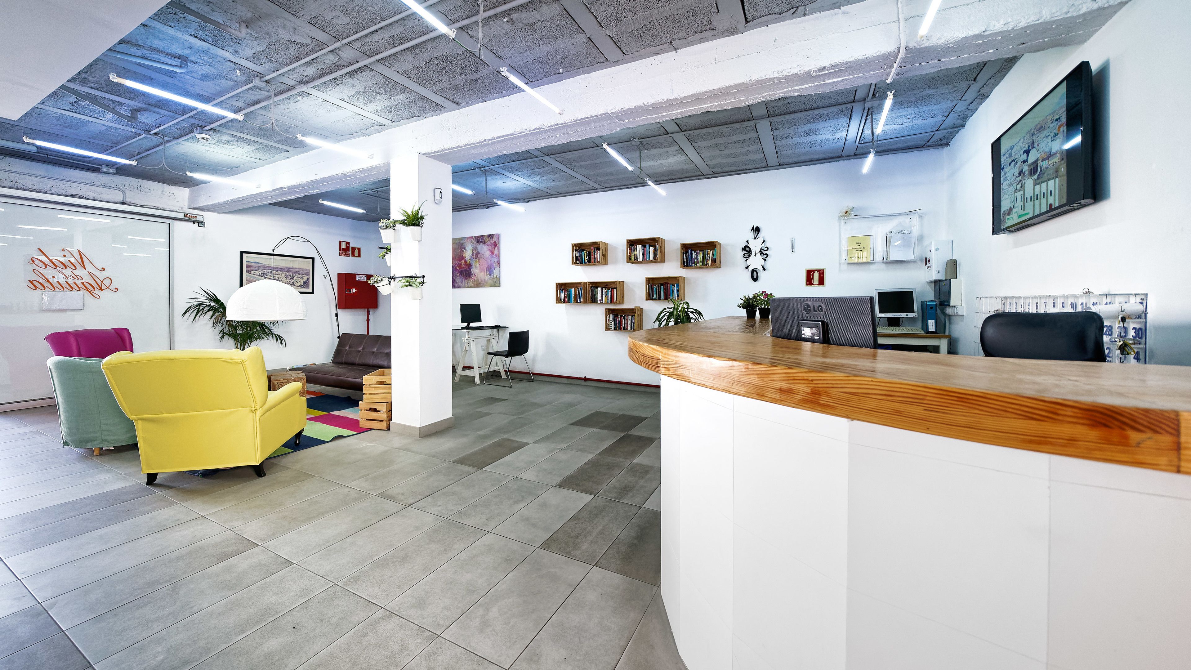 Un espacio de oficina moderno con un mostrador de recepción, sillas coloridas, una estantería y un reloj en la pared.