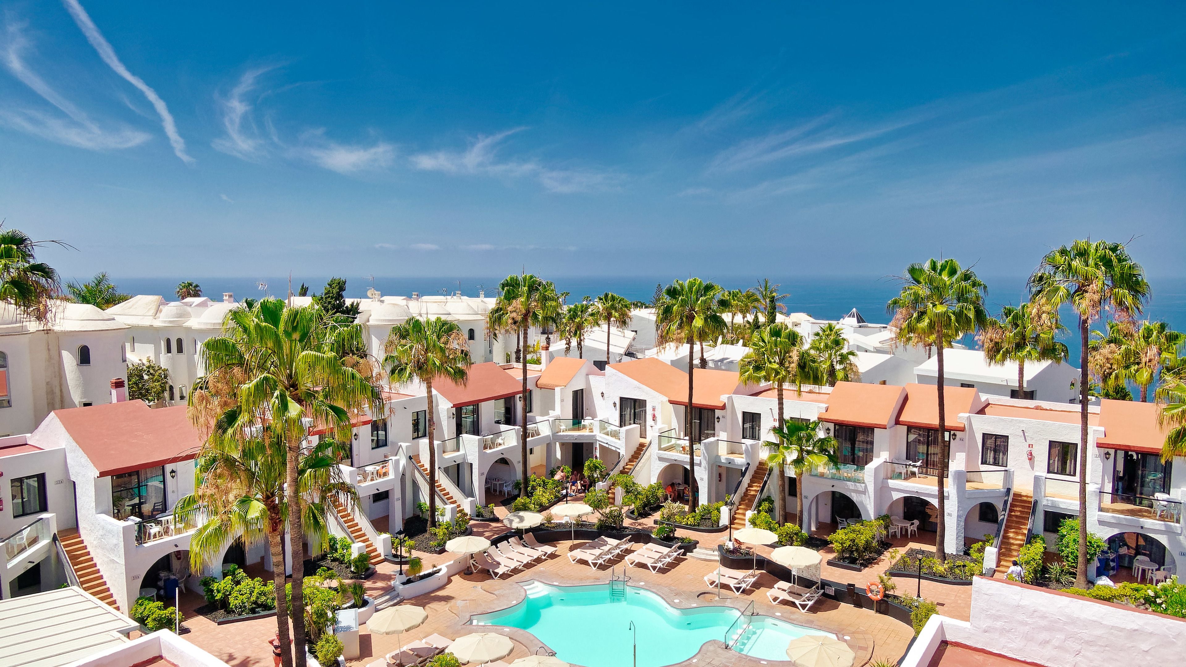 A resort with a central pool, palm trees, and a view of the ocean.
