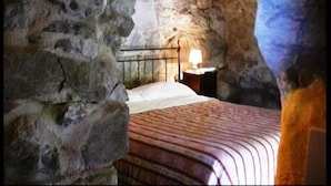 A stone-walled room with a bed, a nightstand, and a lamp. - Agriturismo Al Marnich (Schignano)