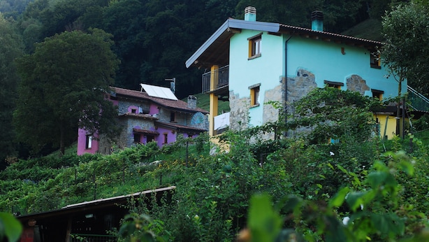 A multi-story building with a stone facade and a flat roof, surrounded by lush greenery and trees. - Agriturismo Al Marnich (Schignano)