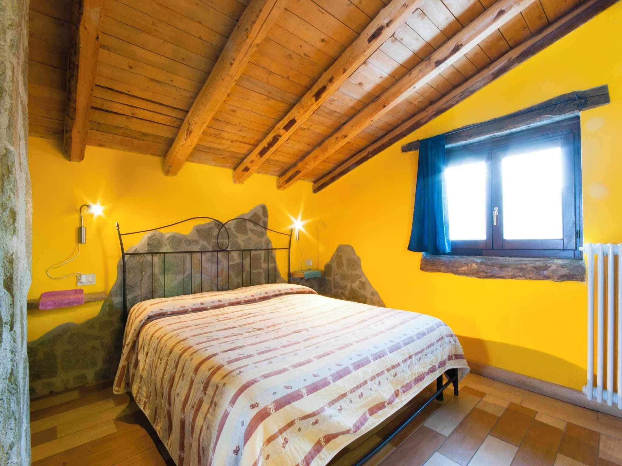 Un dormitorio con techo de madera, cama con colcha estampada, pared de piedra y ventana con cortinas.