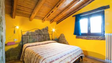 Un dormitorio con techo de madera, cama con colcha estampada, pared de piedra y ventana con cortinas.