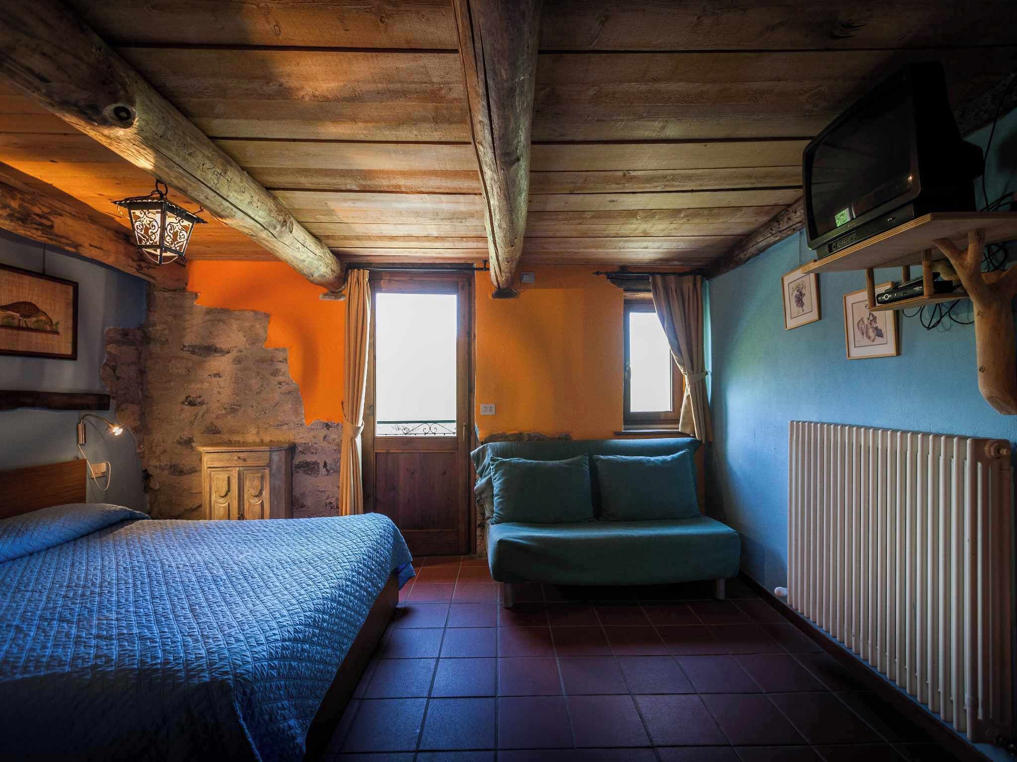 Ein rustikaler Raum mit Holzboden, einem Bett mit blauer Bettdecke, einem grünen Sofa, einem Holzschrank und einem Fernseher auf einem Holzboden.