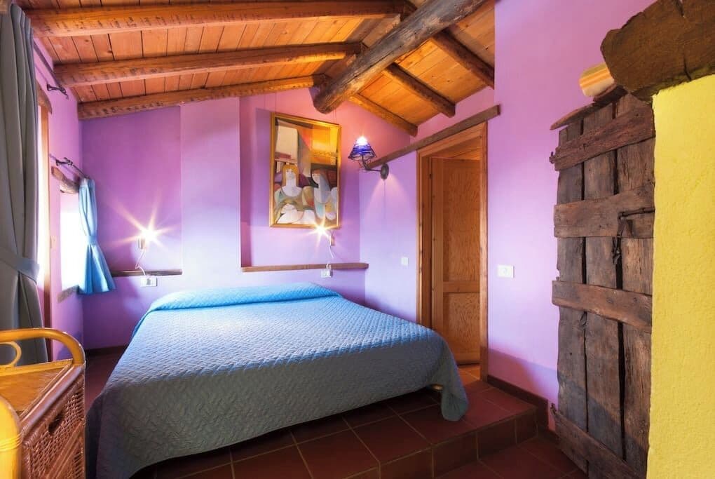 Un dormitorio con cama, vigas de madera en el techo, un espejo colgado en la pared y una puerta rústica.