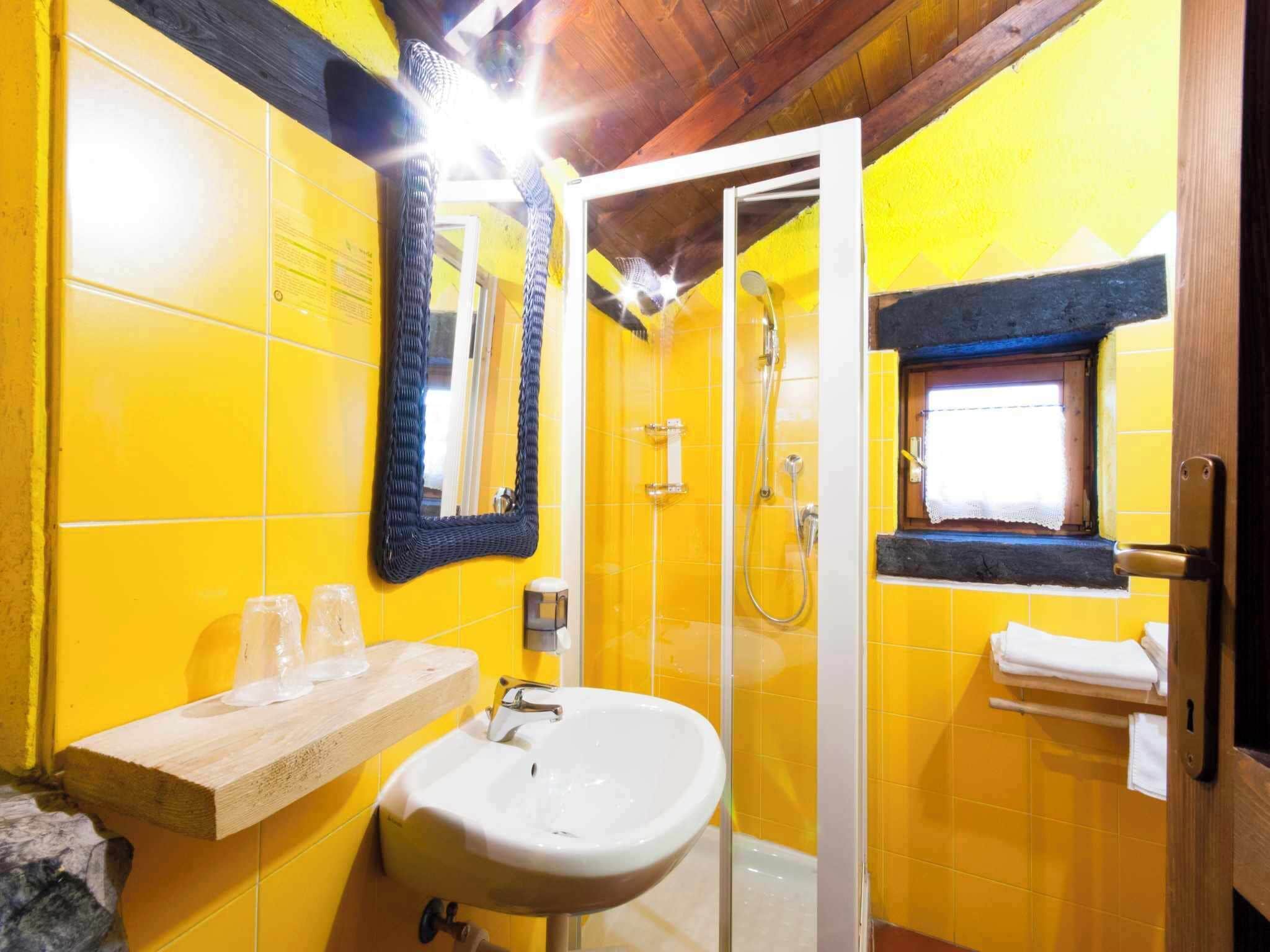 Un baño con azulejos amarillos, un lavamanos blanco, un espejo, una ducha y una ventana con toallero.