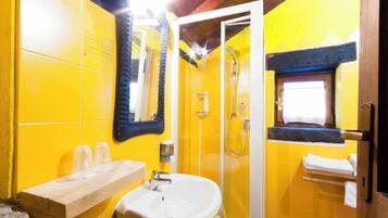 Un baño con azulejos amarillos, un lavamanos blanco, un espejo, una ducha y una ventana con toallero.