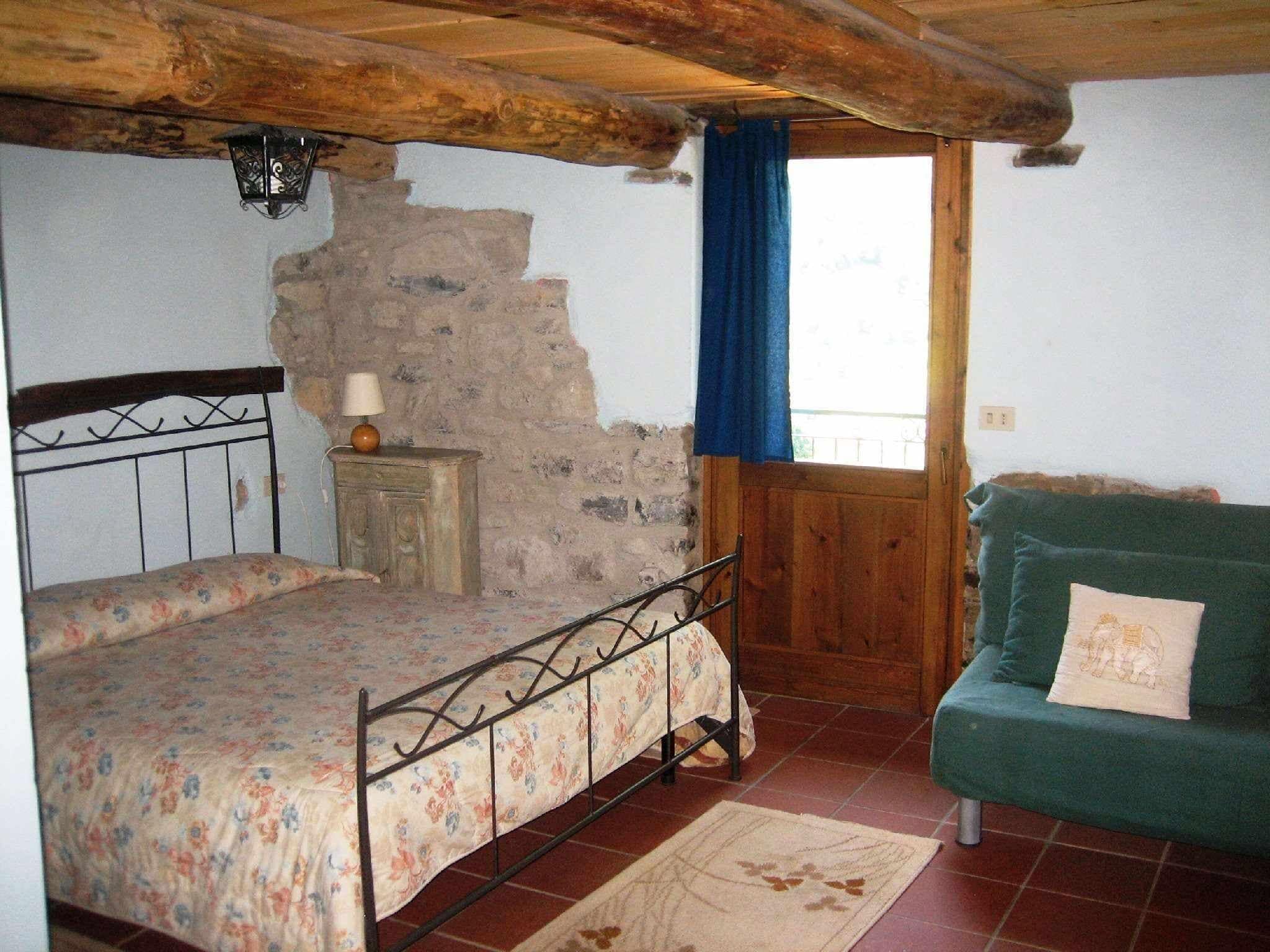 A rustic bedroom with a bed, a wooden dresser, a green sofa, and a stone wall.