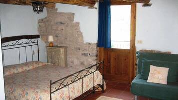 A rustic bedroom with a bed, a wooden dresser, a green sofa, and a stone wall.