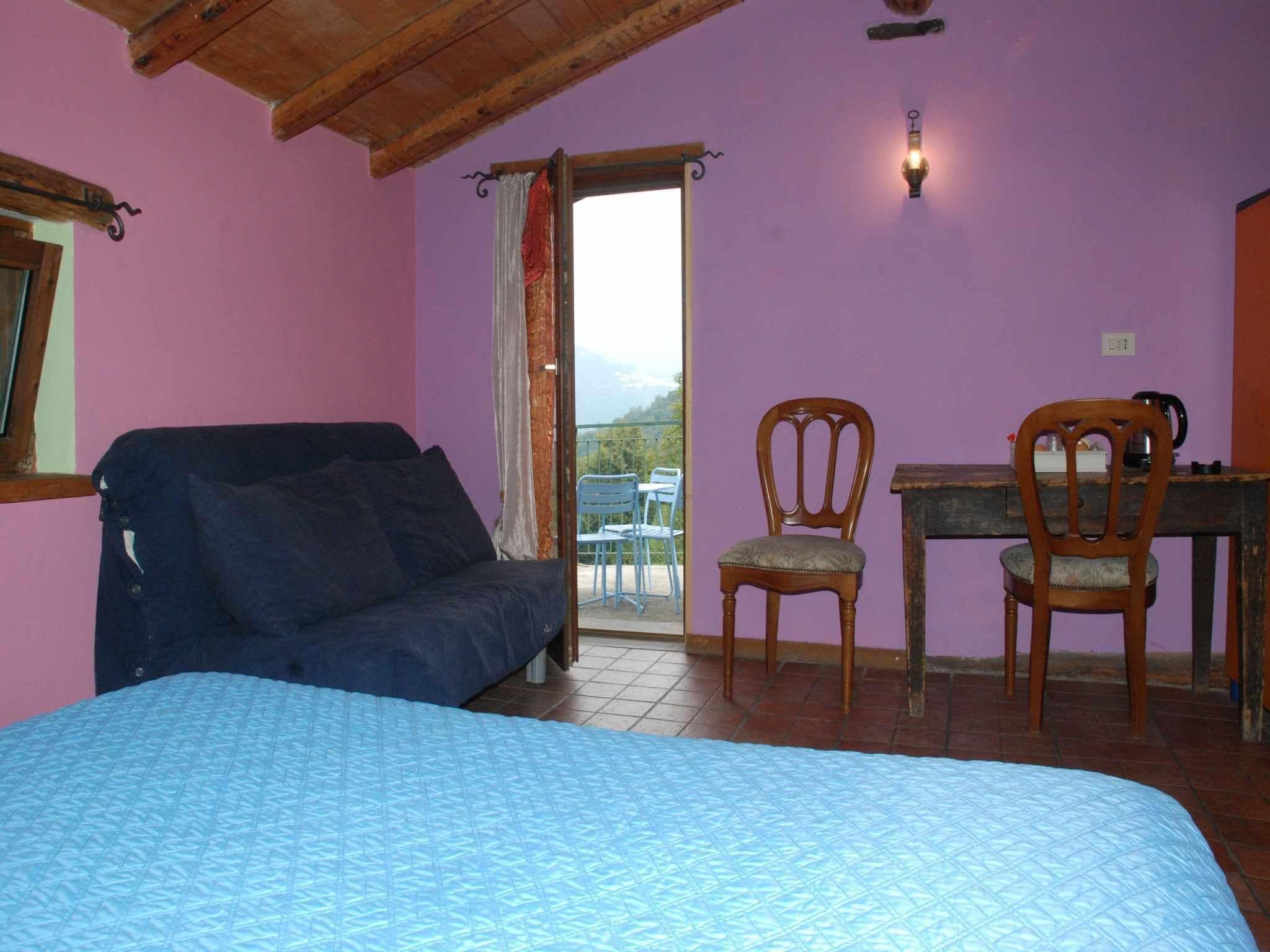 A room with a bed, a wooden desk, two chairs, and a balcony with a view.