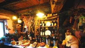 A rustic bar area with wooden shelves stocked with bottles, a teddy bear decoration, and various food items on the counter. - Agriturismo Al Marnich (Schignano)