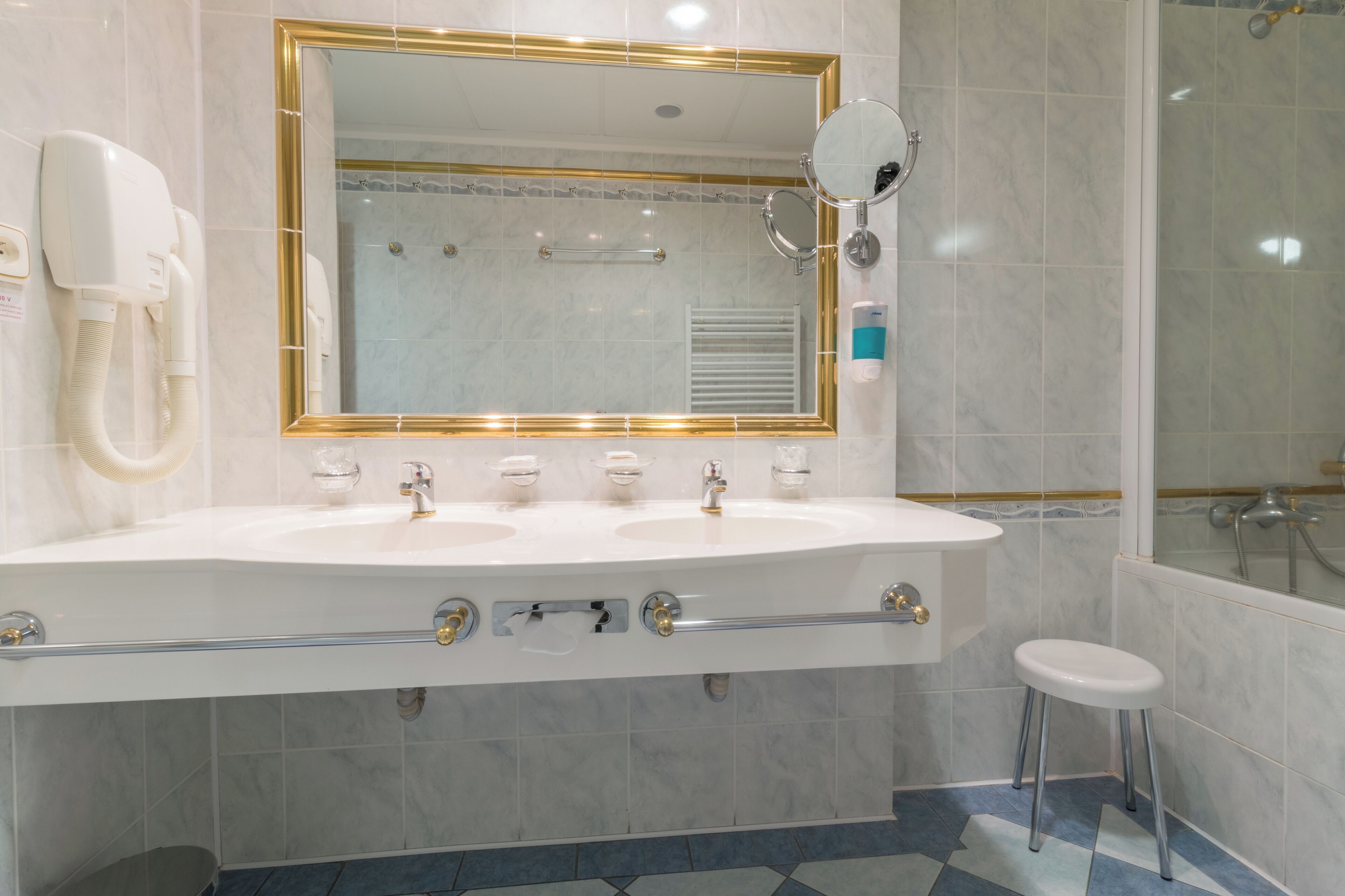 Ein Badezimmer mit einem Doppelwaschbecken, einem Spiegel, einer Duschbrause und einer Toilette.
