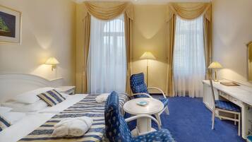 A hotel room with a bed, two chairs, a desk, and a small table.