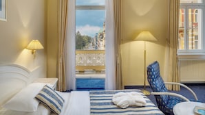 Habitación de hotel con cama, dos lámparas, una silla y vistas a un balcón con edificios.