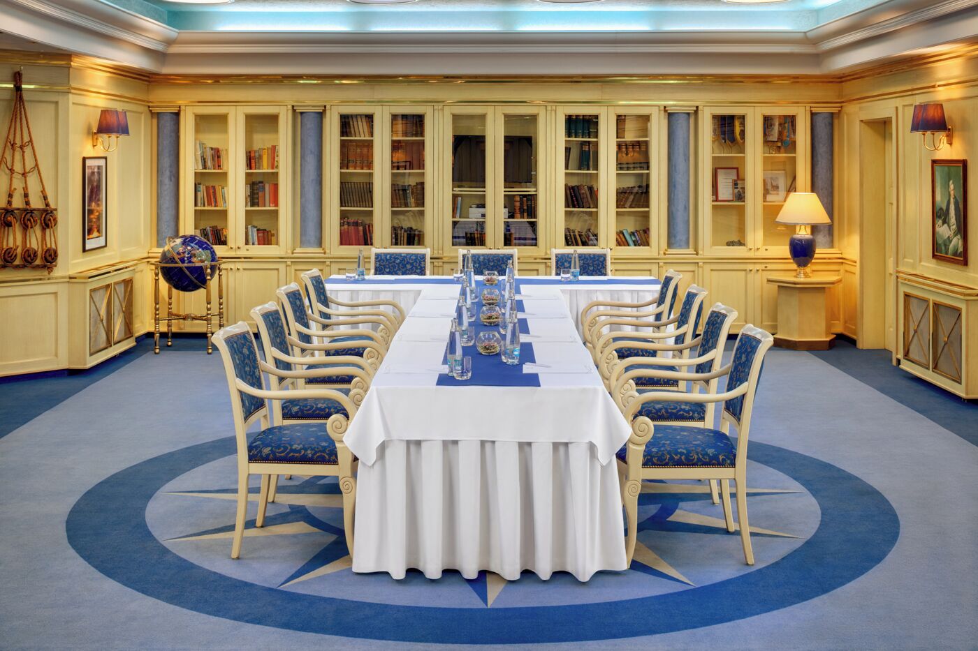 Una sala de reunions formal amb una taula llarga, cadires tapissades de blau i prestatgeries al fons.