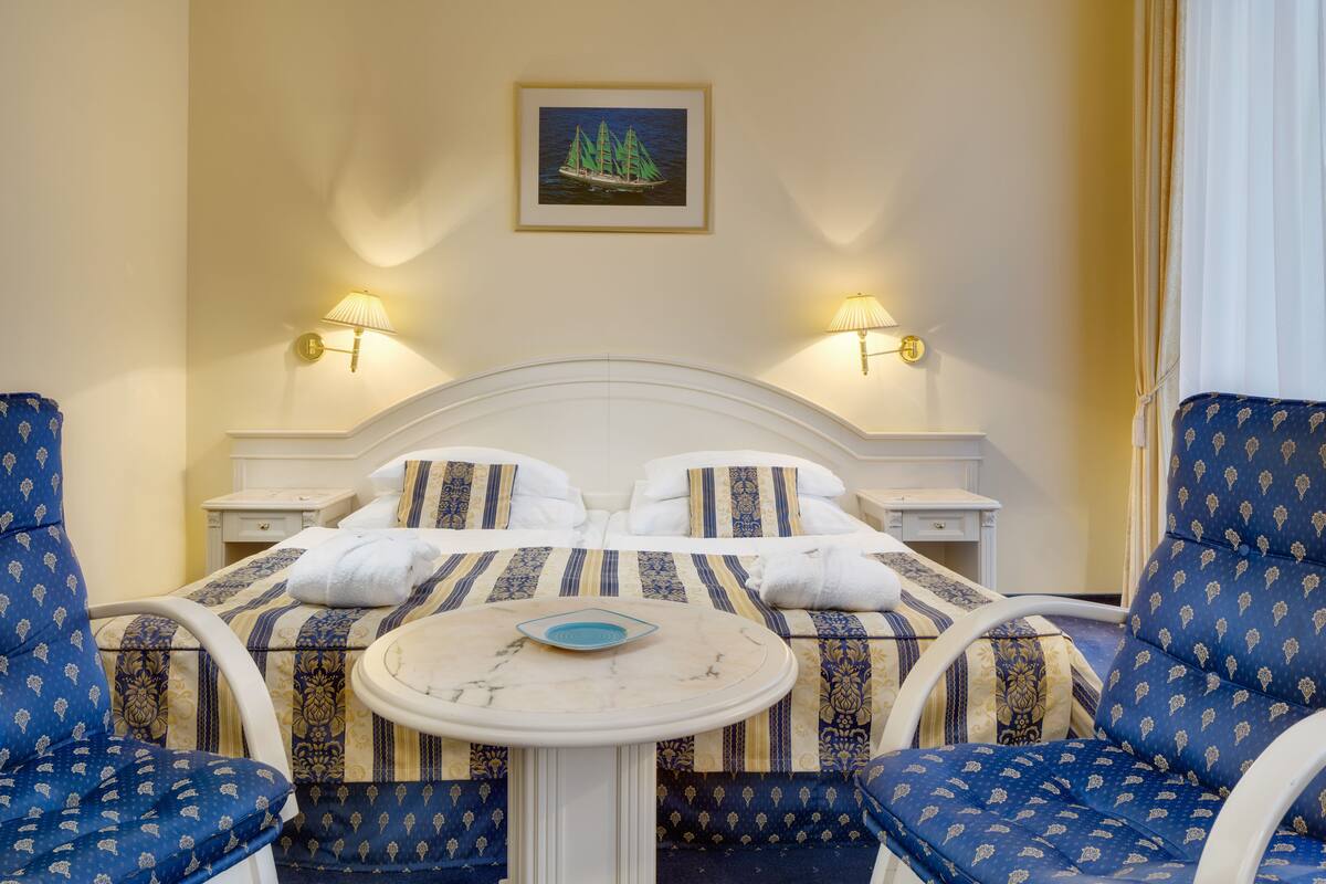 Habitación de hotel con cama, dos sillones, una mesita redonda y dos lámparas de pared.