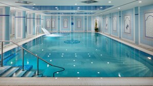 Una gran piscina interior con agua cristalina y paredes de azulejos, bajo un techo con iluminación empotrada.