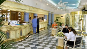 Zona de recepción de hotel con mostrador de check-in, escritorio de recepción y un área de estar con mesa y sillas.