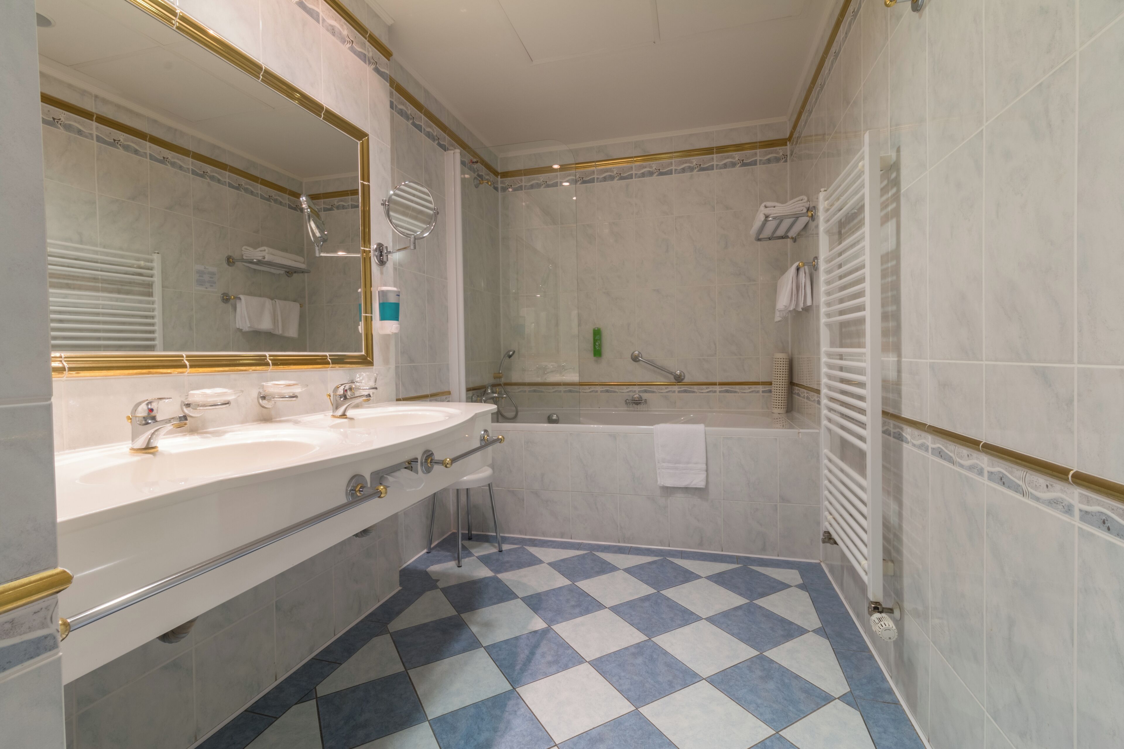 A bathroom with a checkered floor, a large mirror, a bathtub, and a shower area.