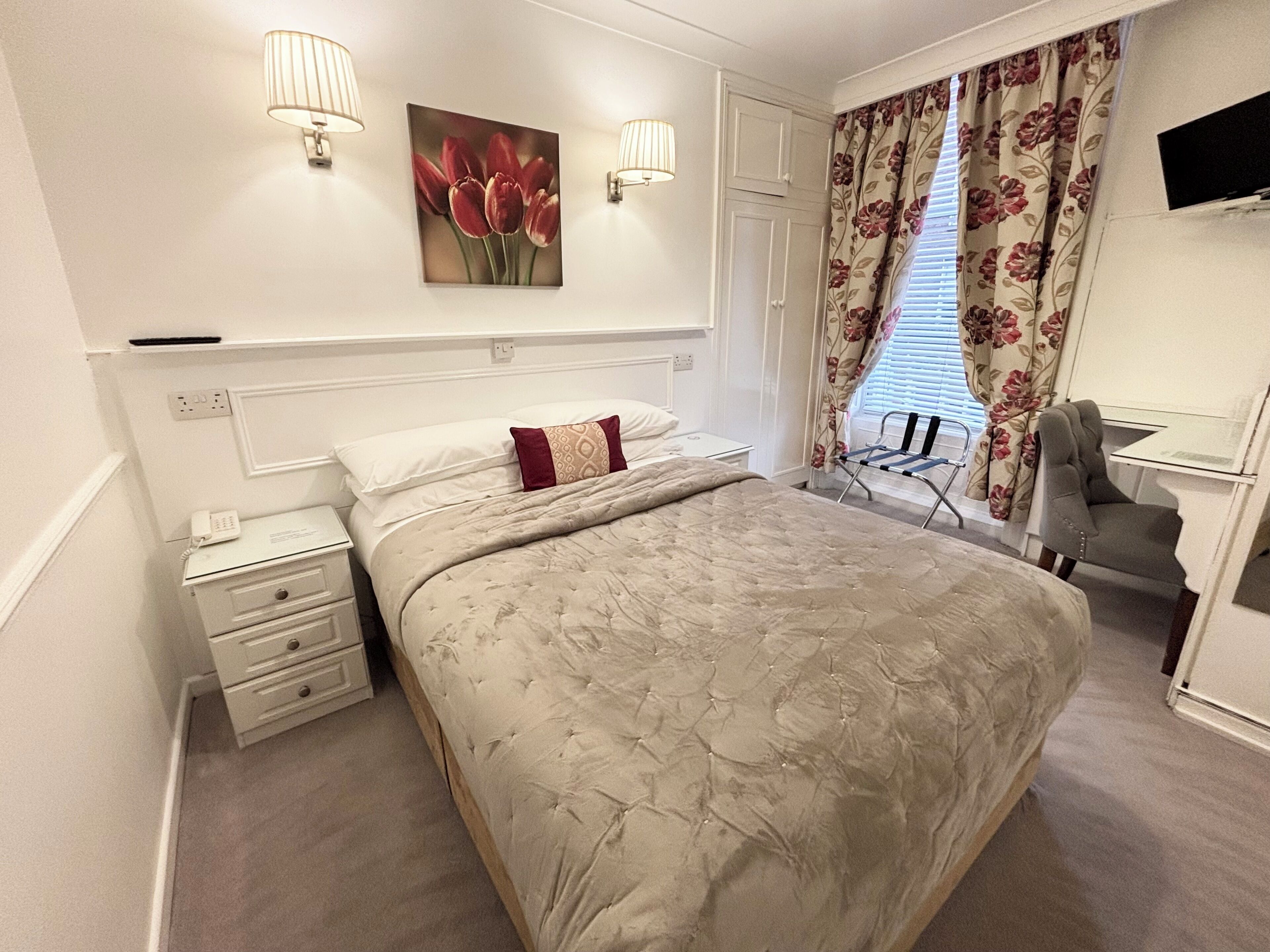 A neatly arranged bedroom with a large bed, bedside tables, a desk, and a chair.