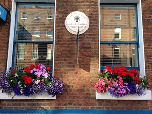 A building facade with two windows, each with a flower box containing a variety of flowers. A plaque is mounted on the wall between the windows. - Dergvale Hotel (Dublin)