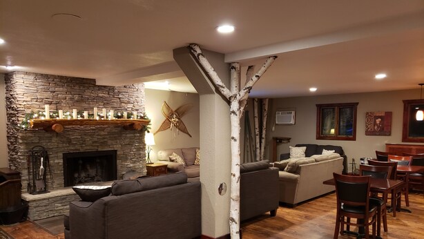 A cozy living room with a stone fireplace, a large tree trunk pillar, and a dining area with wooden chairs and tables. - Rib Mountain Inn (Wausau)