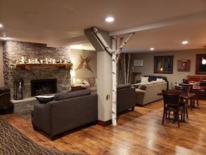 A cozy living room with a stone fireplace, a large tree trunk pillar, and a dining area with wooden chairs and tables. - Rib Mountain Inn (Wausau)