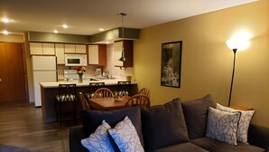 A modern living room with a dark brown sofa, a dining table with chairs, a kitchen area with white cabinets, and a painting on the wall. - Rib Mountain Inn (Wausau)