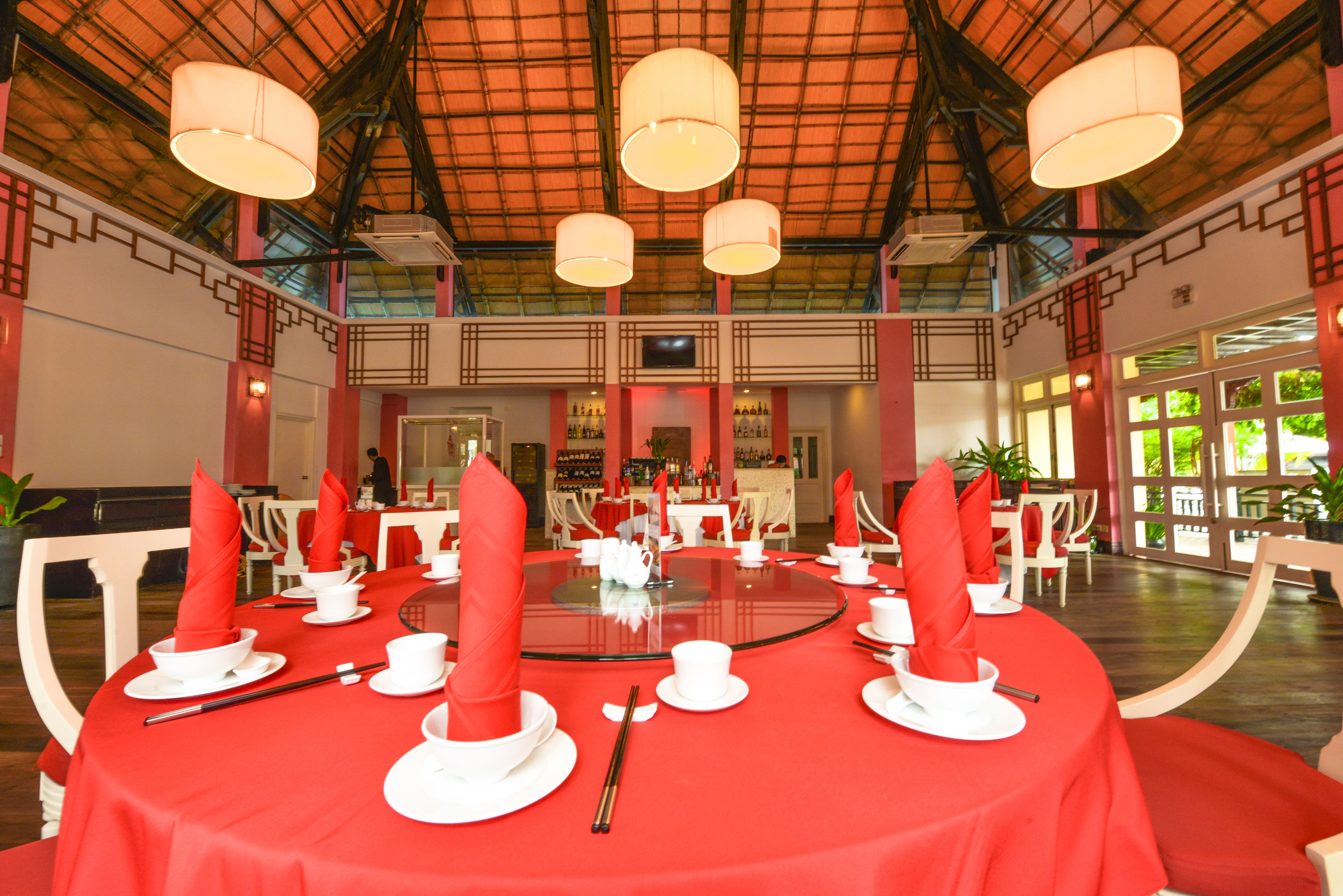 Un espace repas avec des tables rondes dressées pour le service, agrémentées de nappes rouges et de vaisselle blanche.
