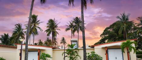 A hotel with a two-story structure, palm trees, and a sunset sky.