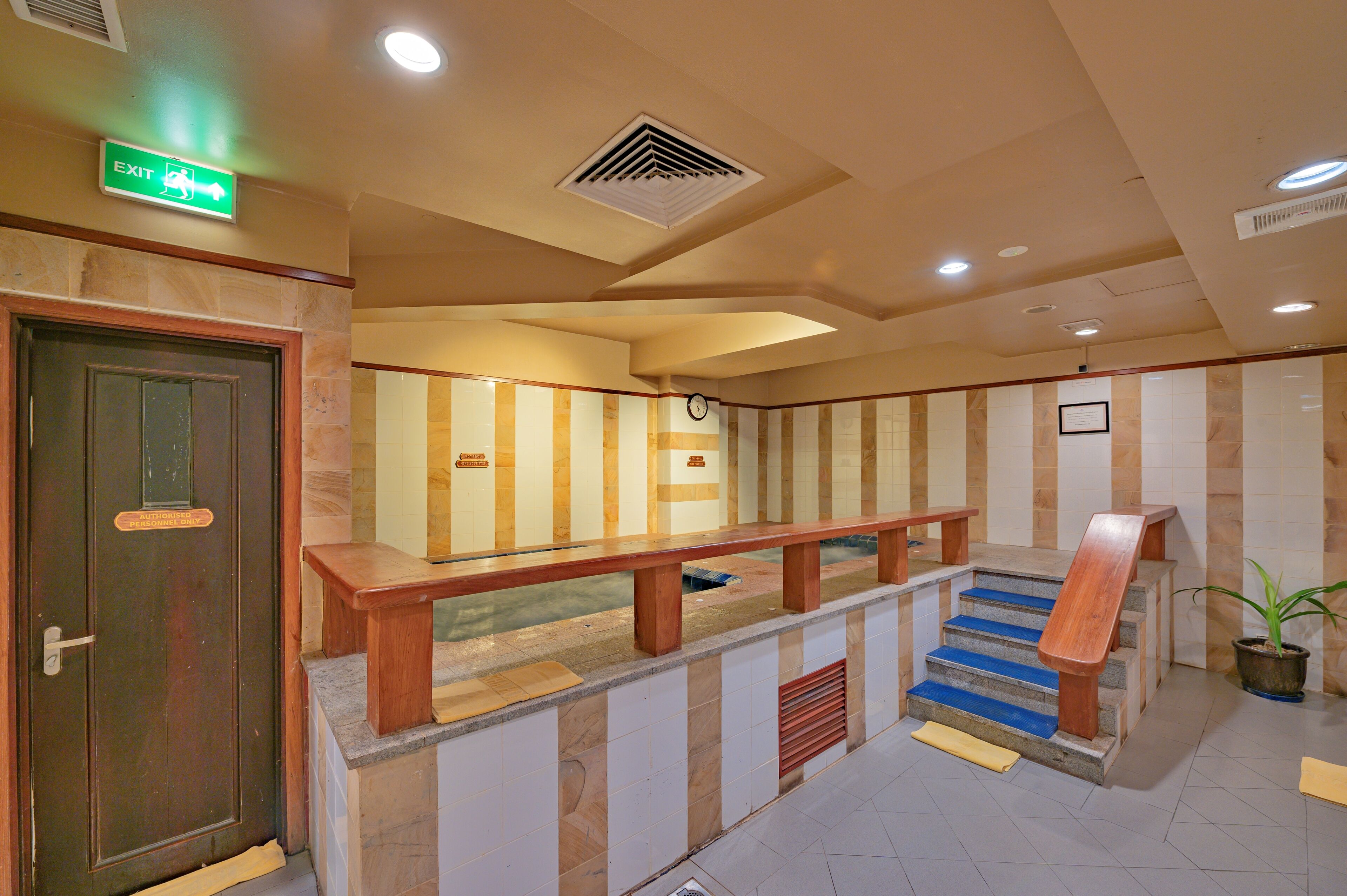 A hotel lobby with a staircase, a reception desk, and a green exit sign.
