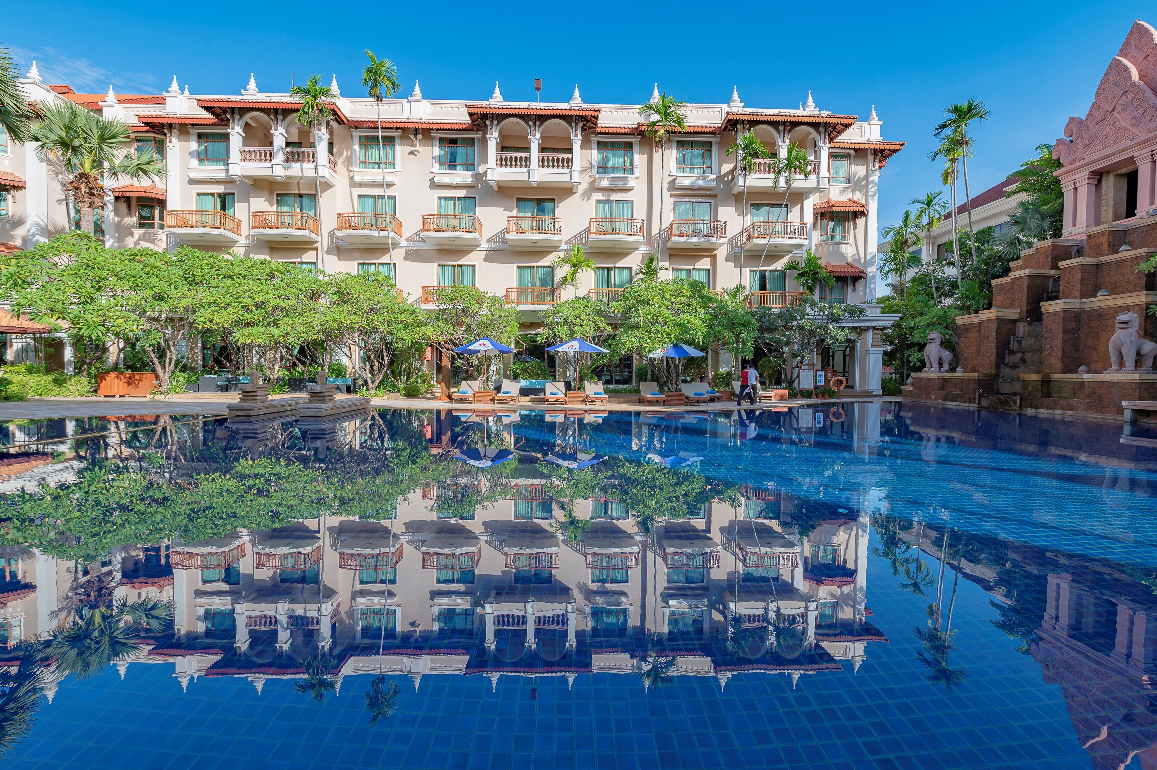 A hotel with a large pool, multiple balconies, and palm trees.