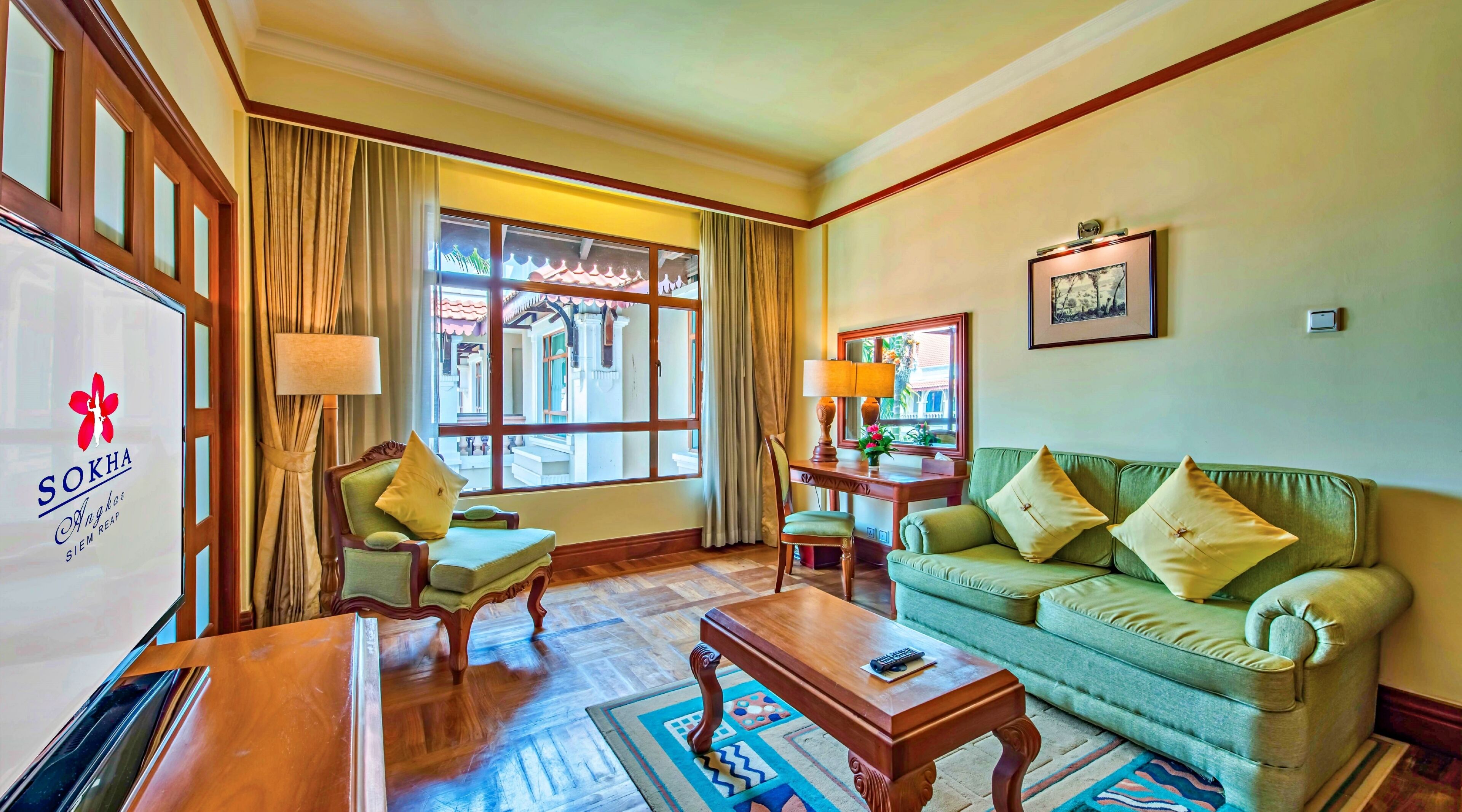 A hotel room with a sofa, armchair, table, and a window with curtains.