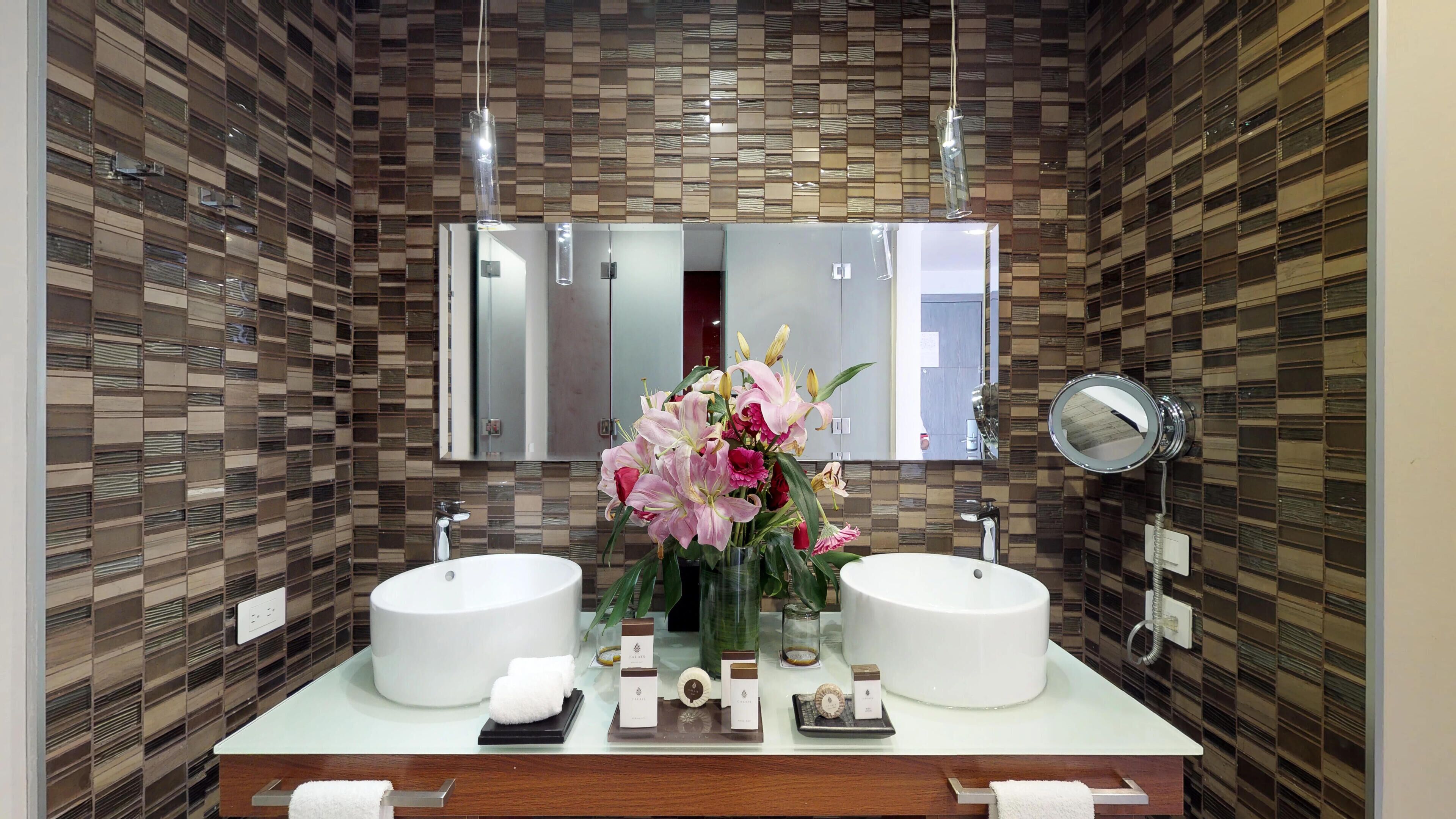 Ein modernes Badezimmer mit zwei Waschbecken, einem großen Spiegel und einer dekorativen Vase mit Blumen.