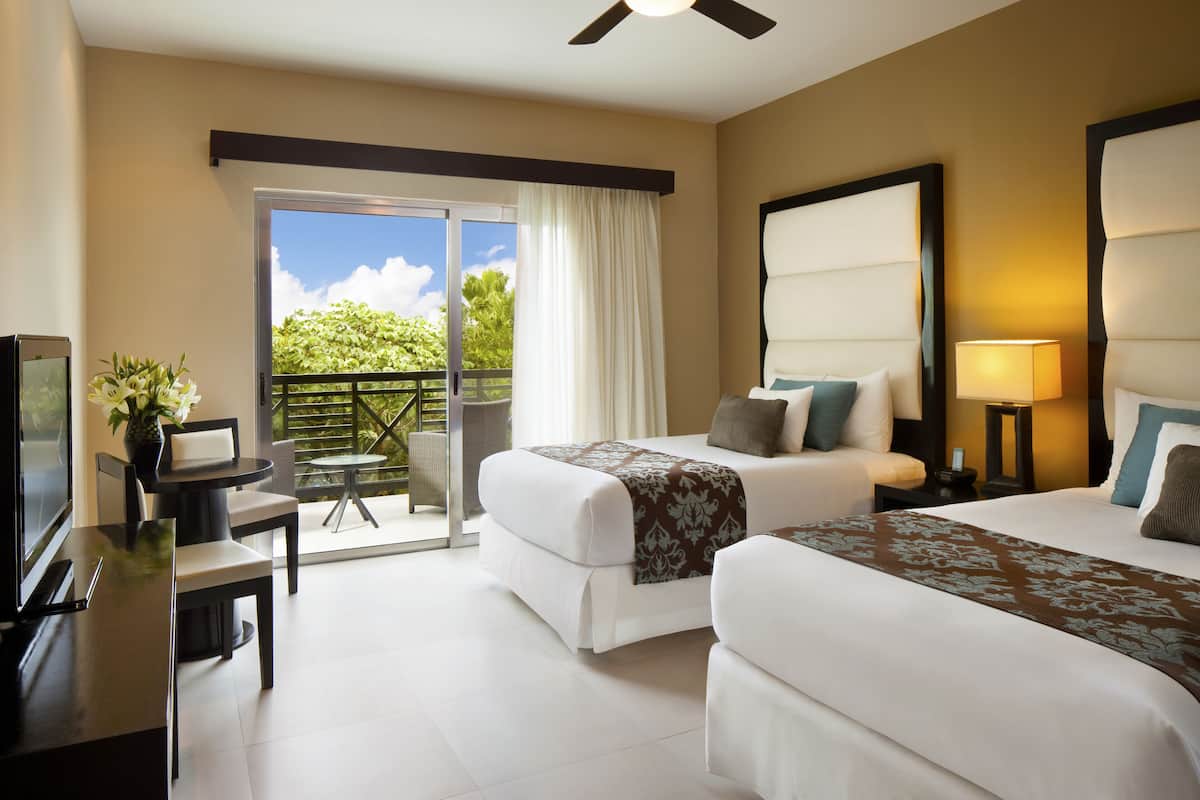 A hotel room with two beds, a balcony, a TV, and a desk with a chair.